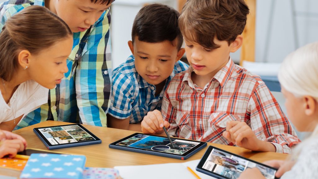 Five young students looking over at one students about to tap on a Lenovo 10w tablet on a table