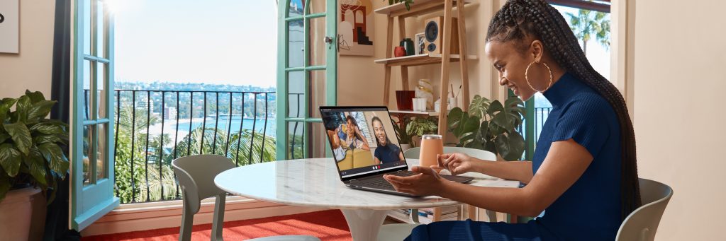 Woman working on an HP Spectre x360 16 at at table in front of a balcony facing the water