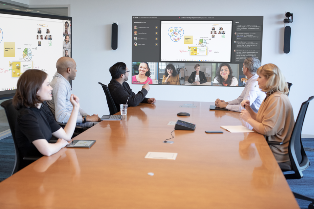 employees seated at table in conference room with virtual attendees