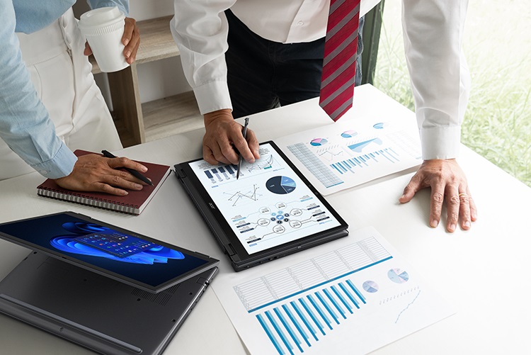 Two people standing over a desk with papers and working on a TravelMate Spin P4 in tablet mode