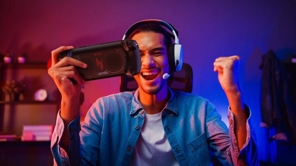 Man wearing over ear headset cheering as he holds handheld gaming device