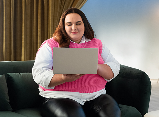 Woman sitting down holding a laptop, back of device facing reader