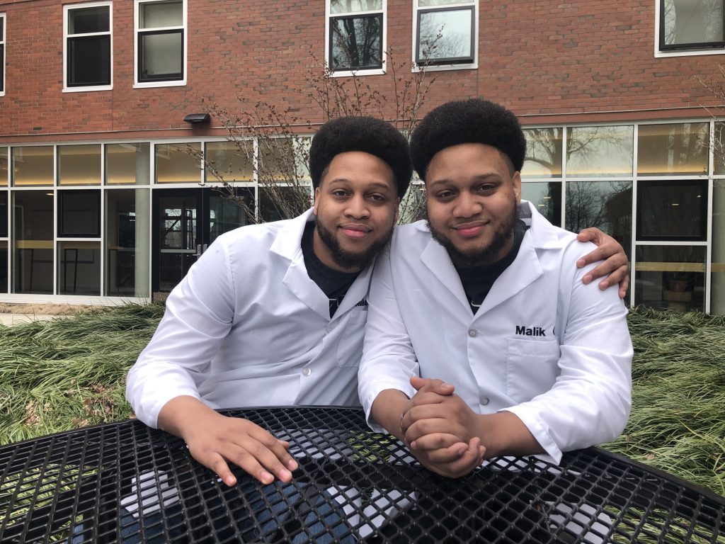 Two men in lab coats sitting next to each other outside