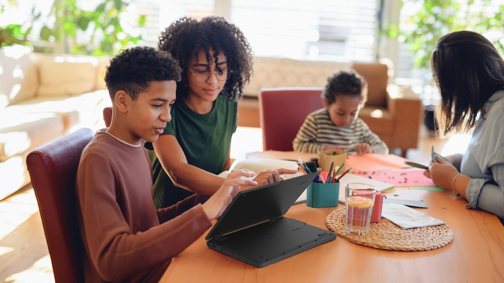 Family at table at home, with two family members looking at laptop screen