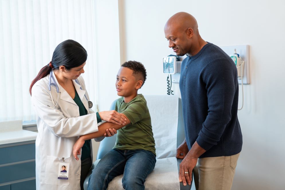 A medical clinician talking with a child and adult in an exam room.