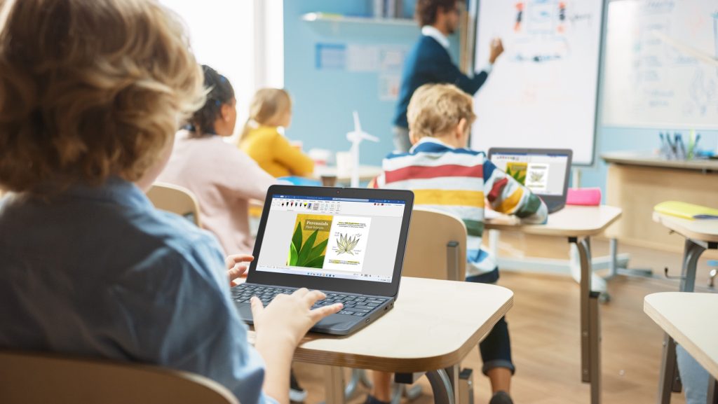 A closeup of a laptop as seen from behind a student in a classroom