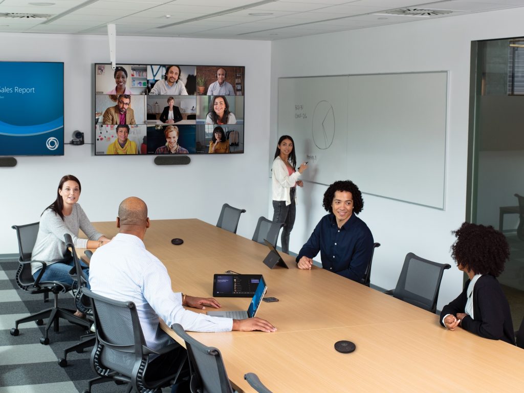 People in an office conference room having a meeting with people on a video Teams call