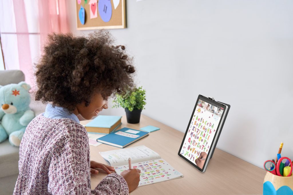 Girl sitting at a desk writing on paper with camera from HP 11-inch tablet showing what she's writing on screen